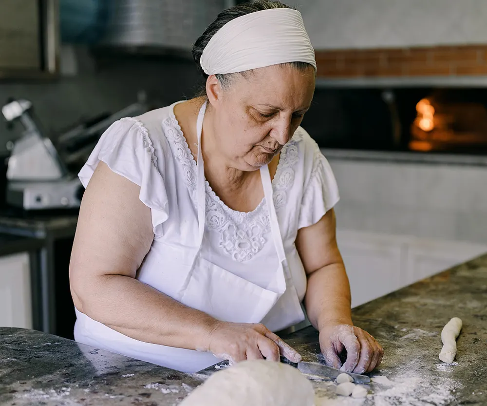La nonna stende l’impasto a mano, con il forno a legna dietro